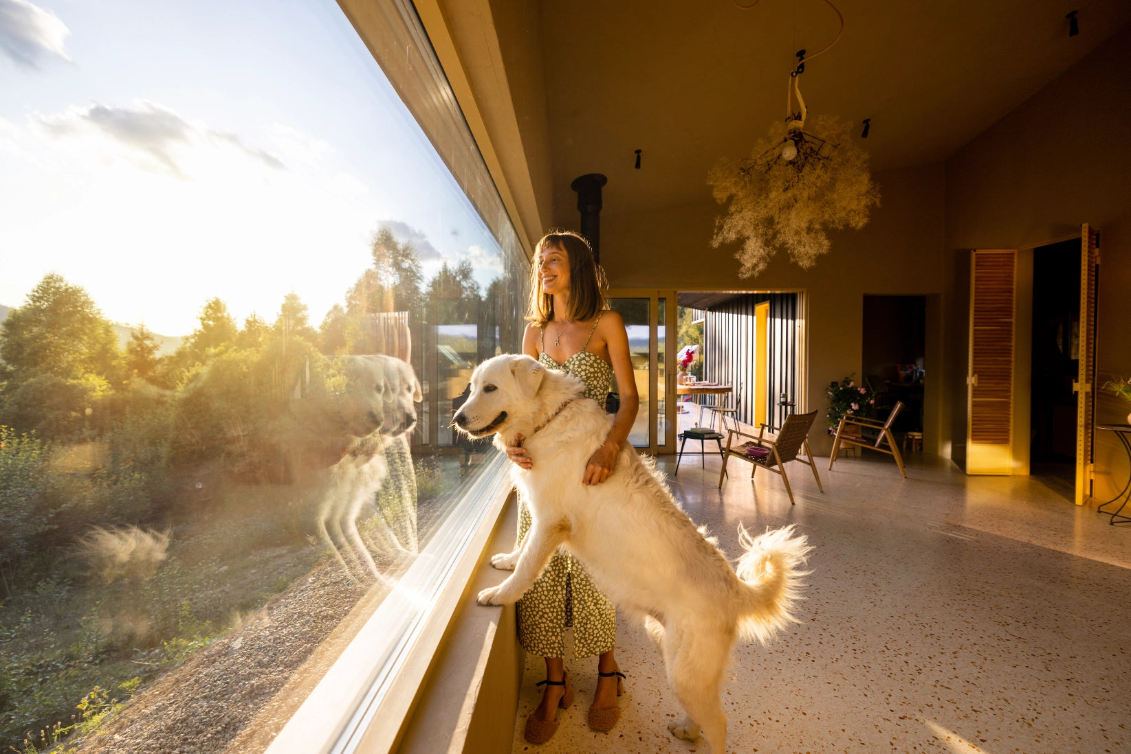 A woman standing next to a dog looking out a window.