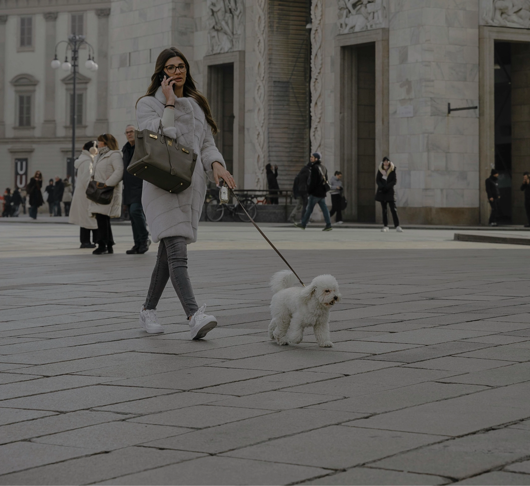 A woman walking a small white dog on a leash.